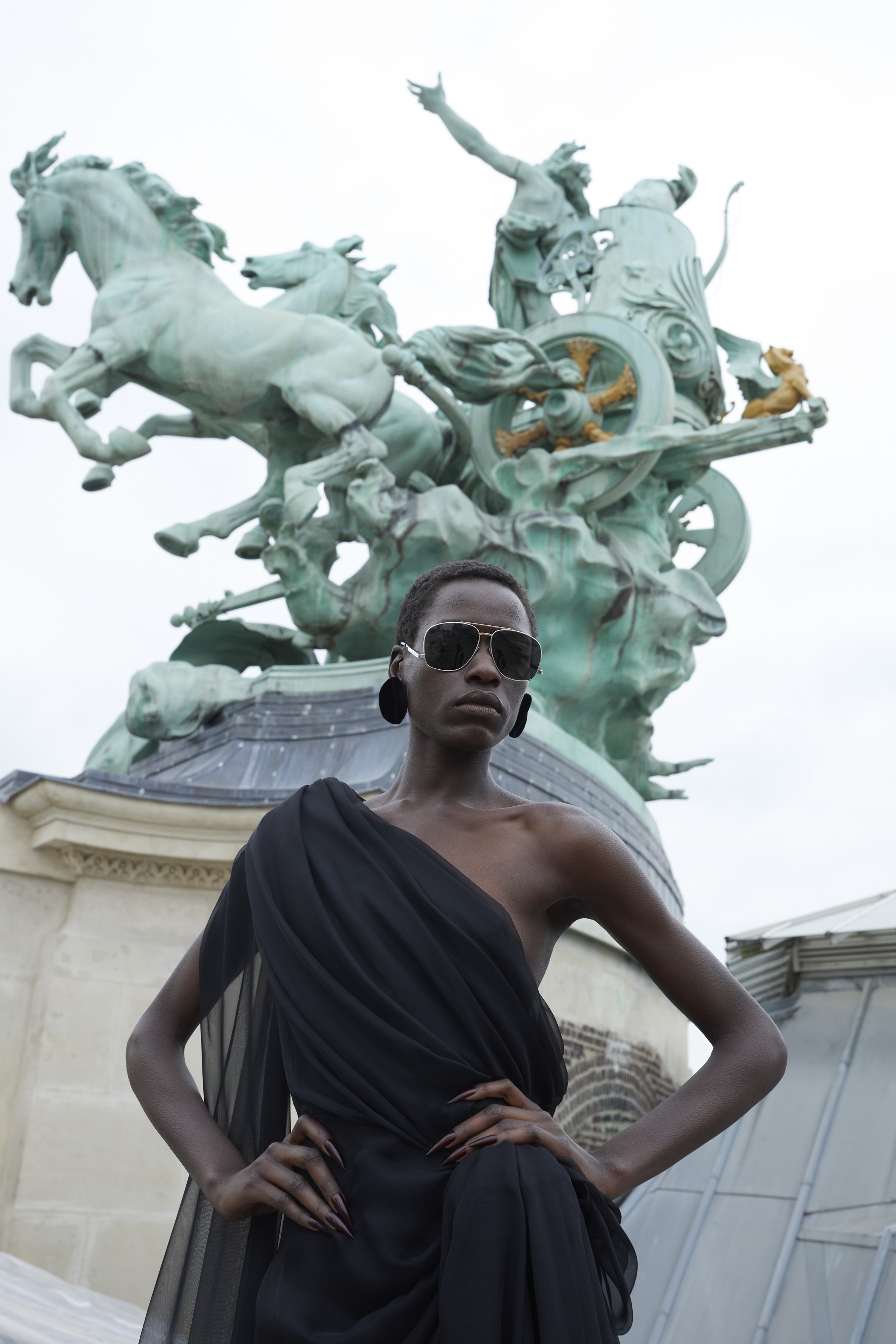 A model in front of a statue wearing a black one shoulder dress
